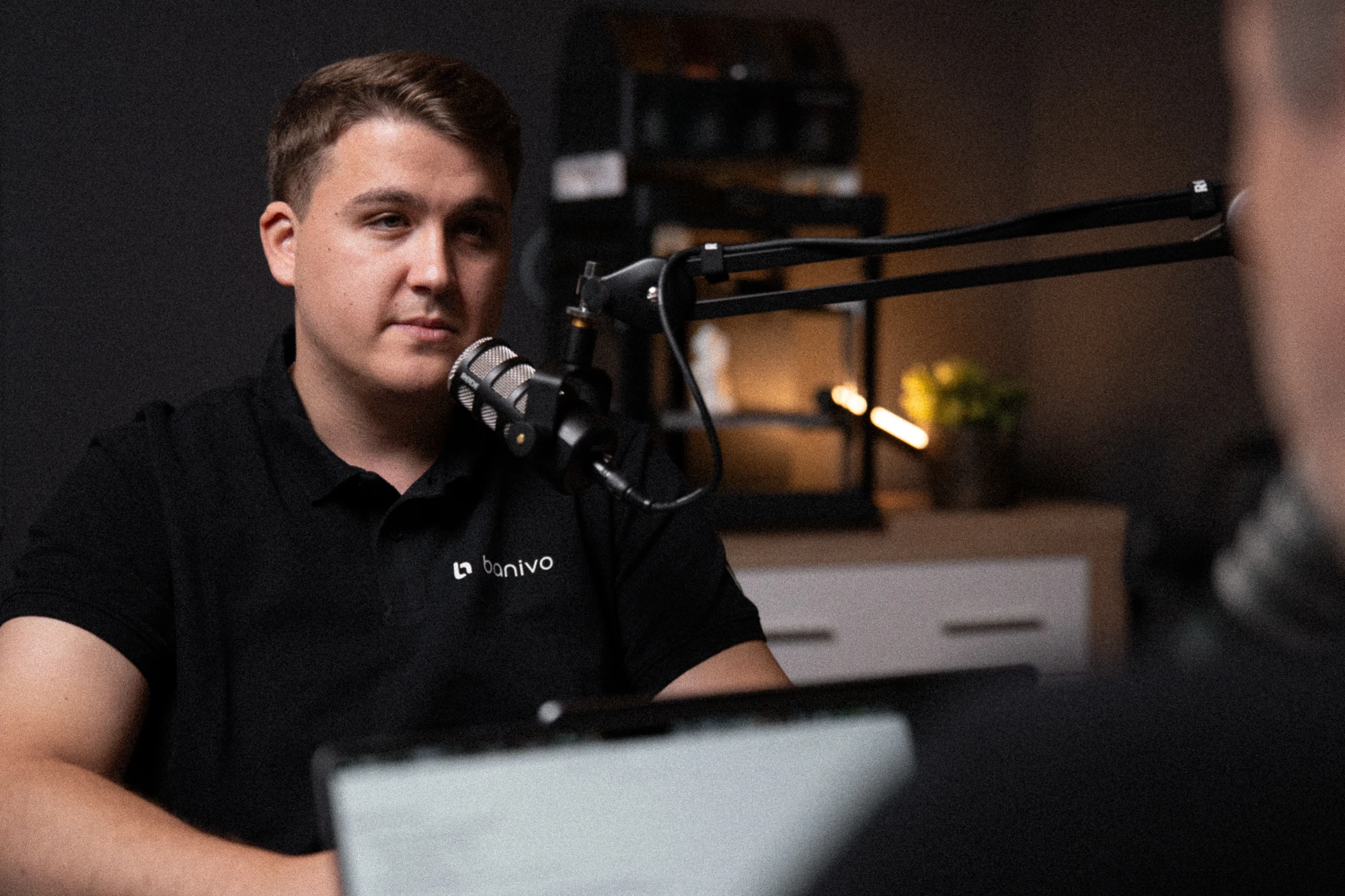 A Banivo Podcast egyik beszélgetőpartnere mikrofonnál, fekete Banivo-pólóban
